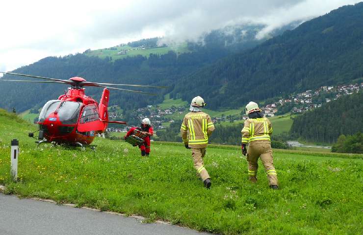 Un elicottero di soccorso alpino in montagna con tre operatori vestiti di riallo e rosso
