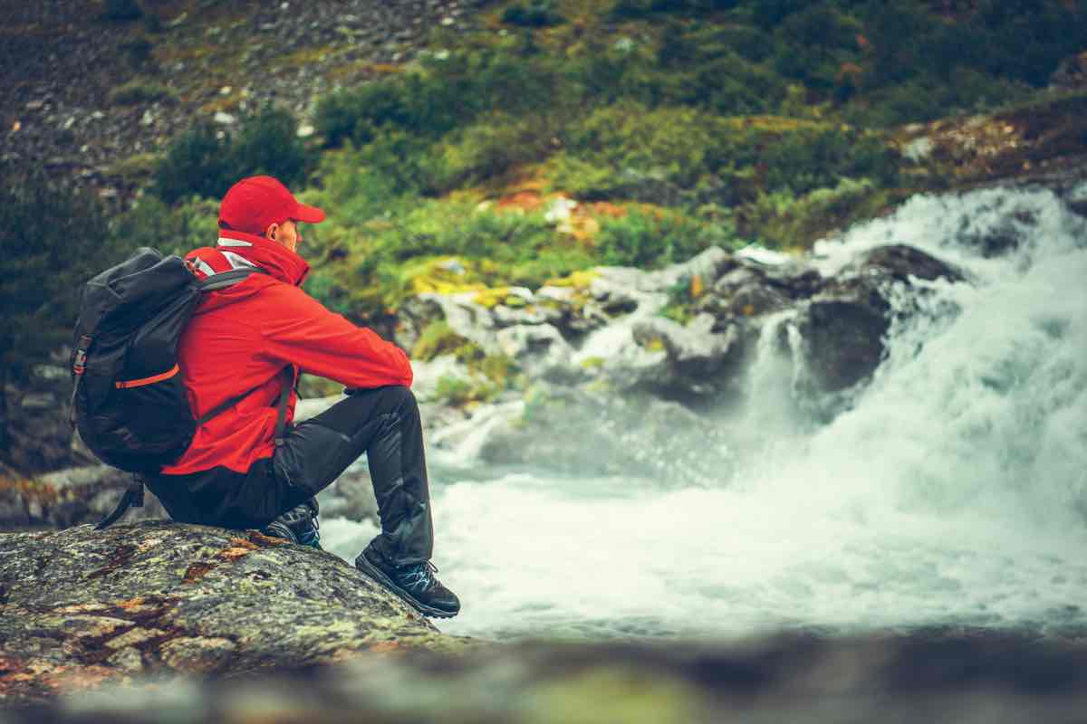 Ragazzo seduto sulla riva di un torrente in tenuta da trekking