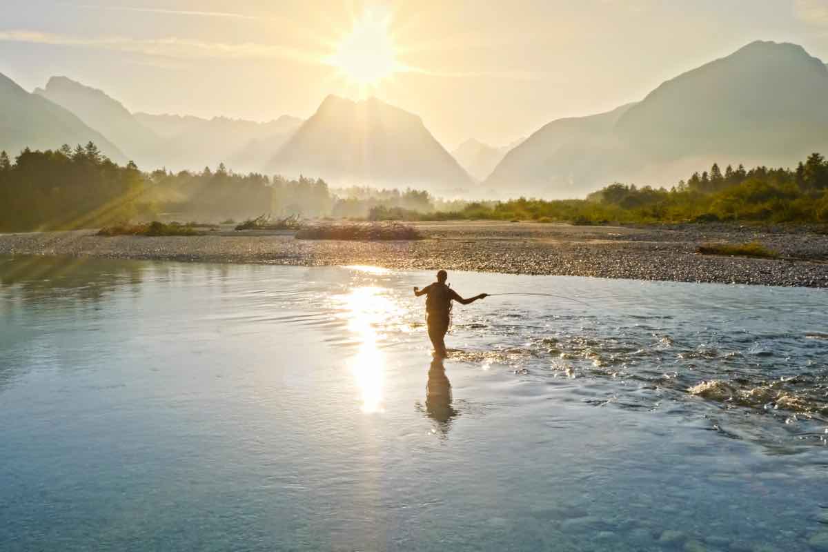 Un uomo pesca al centro di un lago tra le montagne
